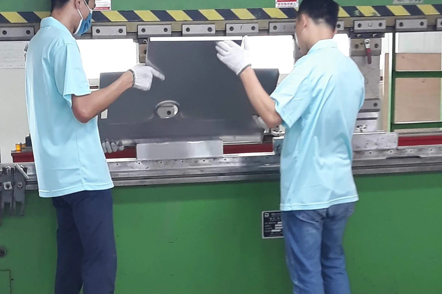 Two operators forming a stainless steel sink bowl on a press brake